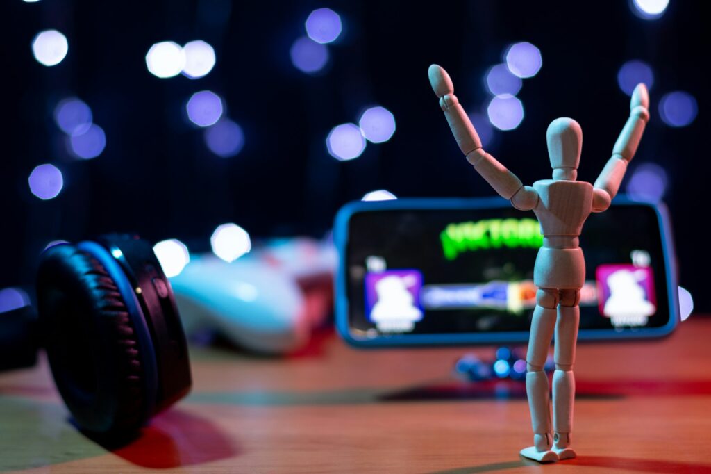 Excited Wooden Articulated Doll Celebrating Victory in Mobile Game with Headphones Nearby