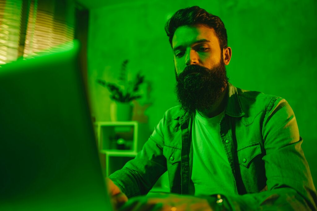 Hardworking full-stack senior developer typing on a laptop in a green-lighted home office.